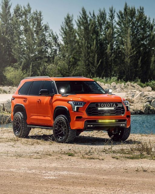 an orange truck parked on the side of a dirt road next to a body of water