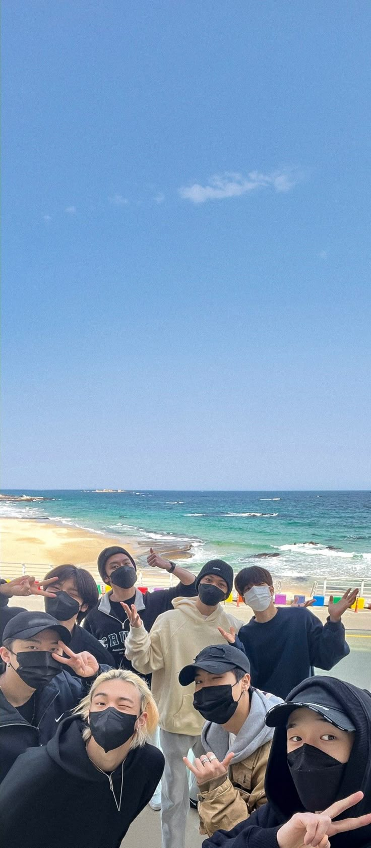 group of people wearing masks standing on beach next to ocean with blue sky in background