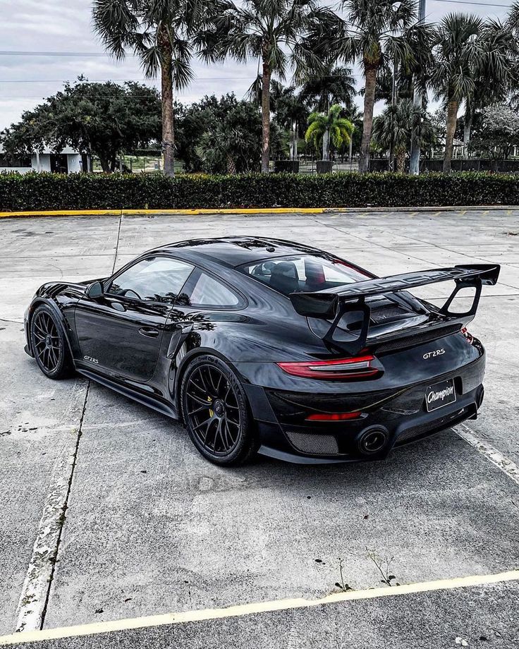 a black porsche sports car parked in a parking lot with palm trees behind it,