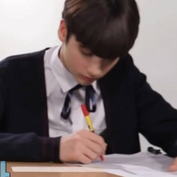 a young boy sitting at a desk writing on paper with a pencil in his hand