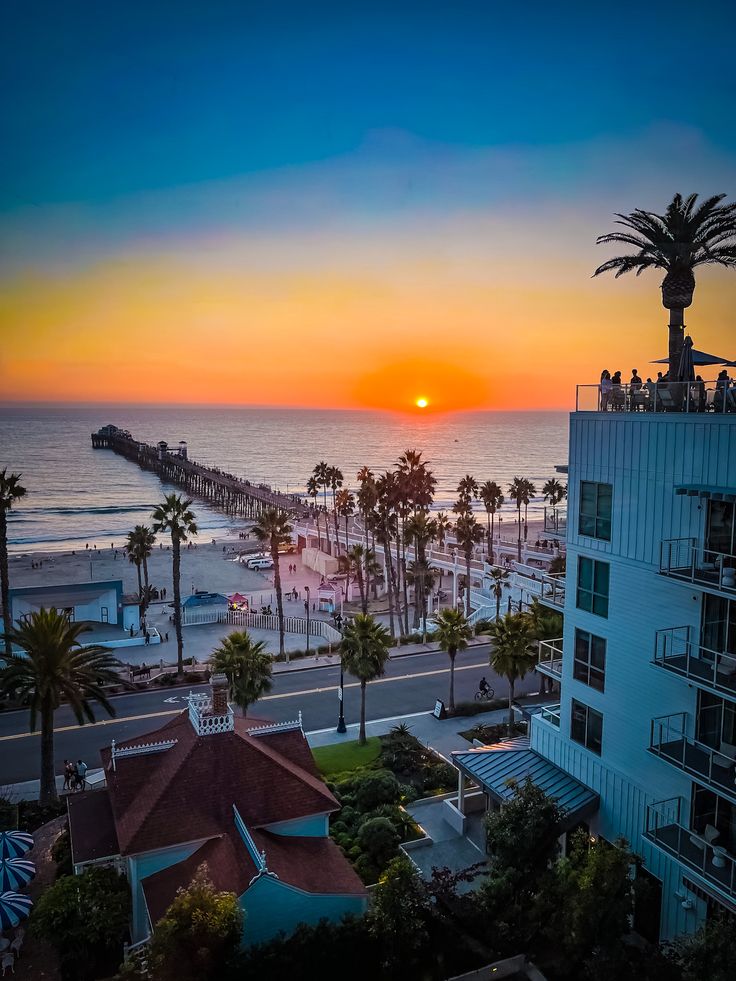 the sun is setting over an ocean and beach with palm trees in front of it