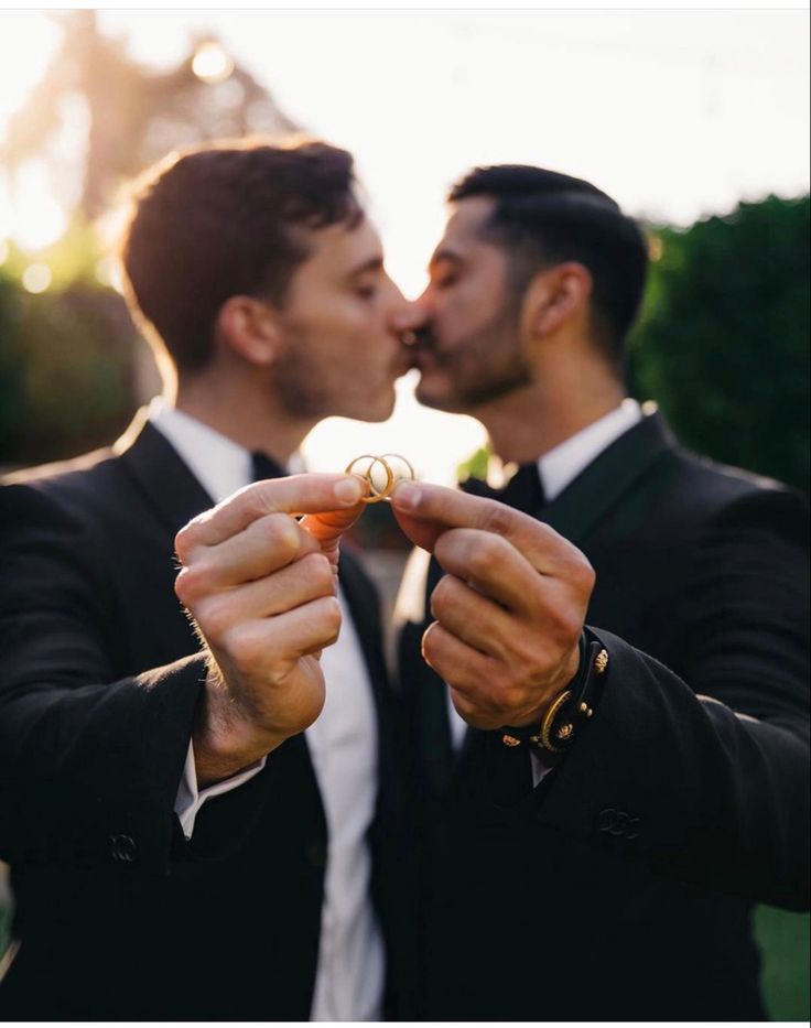 two men in tuxedos are kissing each other with their rings on their fingers