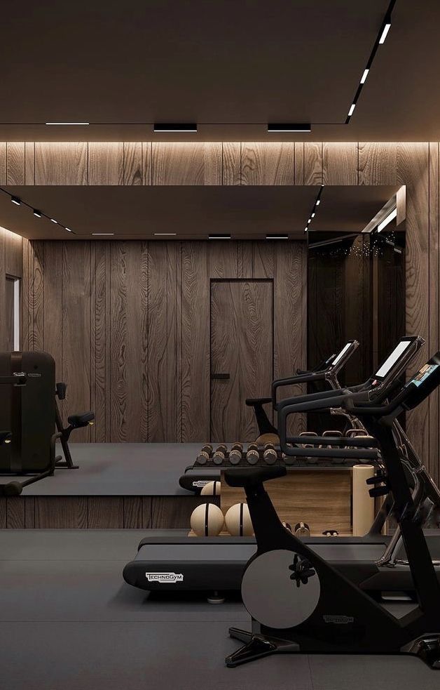 a gym with treadmills, exercise bikes and other equipment in front of a wooden wall