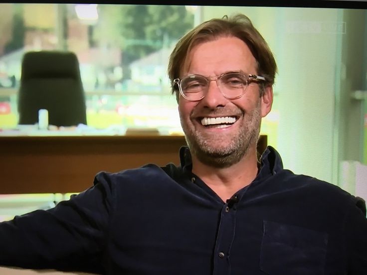 a man with glasses sitting in front of a desk and smiling at the camera,