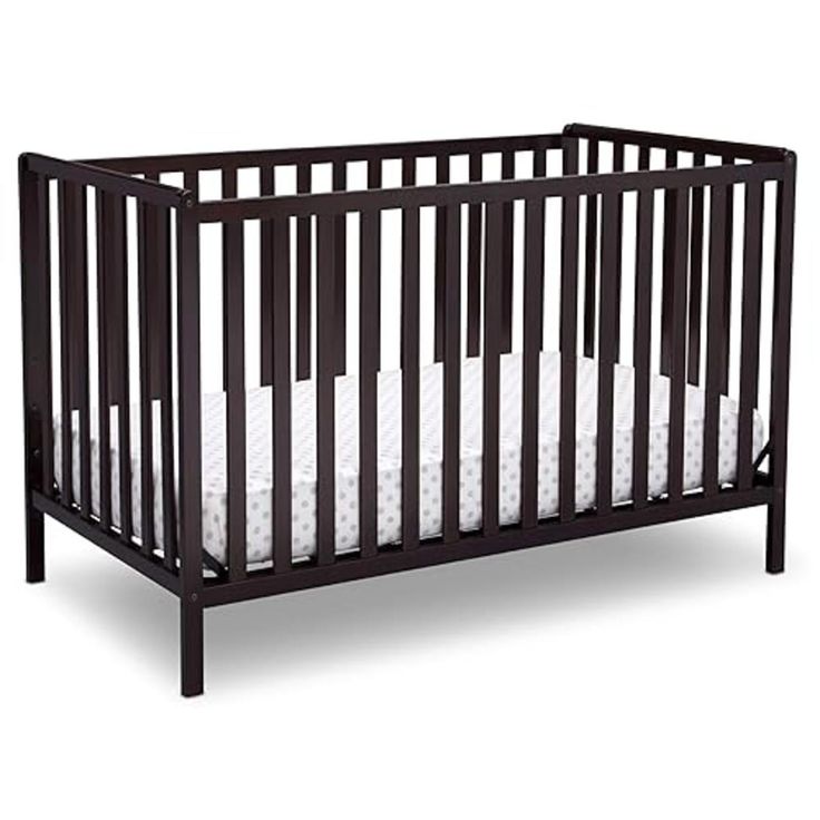 a baby crib with white sheets on the bottom and side rails, in dark wood