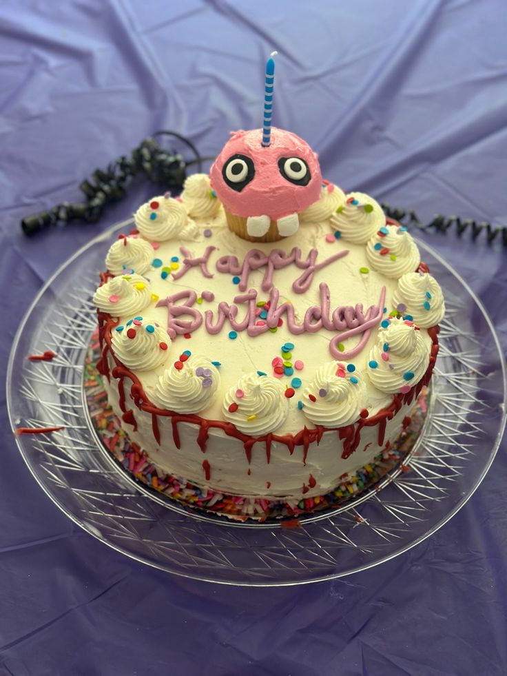 a birthday cake with white frosting and sprinkles is on a clear plate