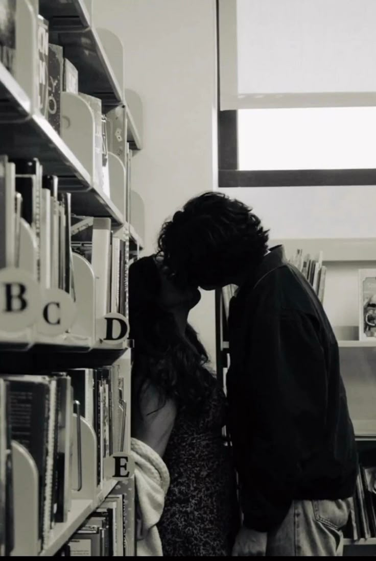 a man and woman kissing in front of a book shelf with books on the shelves