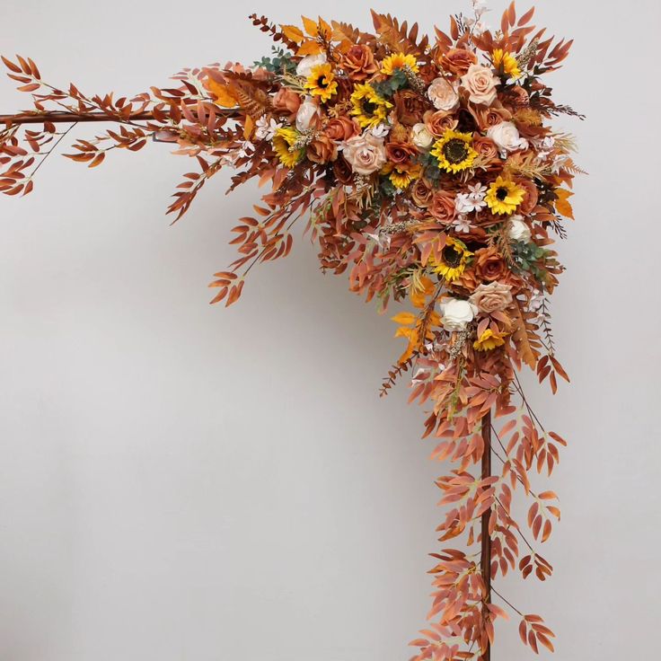 an arrangement of flowers and leaves on a stick in front of a white wall,