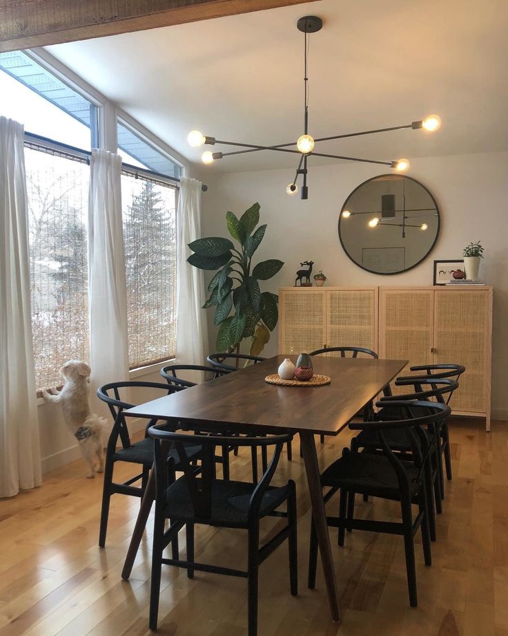 a dining room table with six chairs and a potted plant in the center, next to a large window