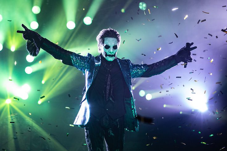 a man dressed as the joker on stage with his hands in the air while confetti falls around him