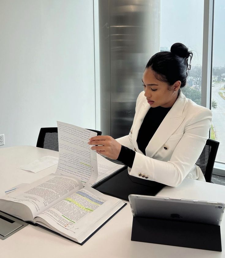 a woman sitting at a table with an open book in front of her, reading the bible