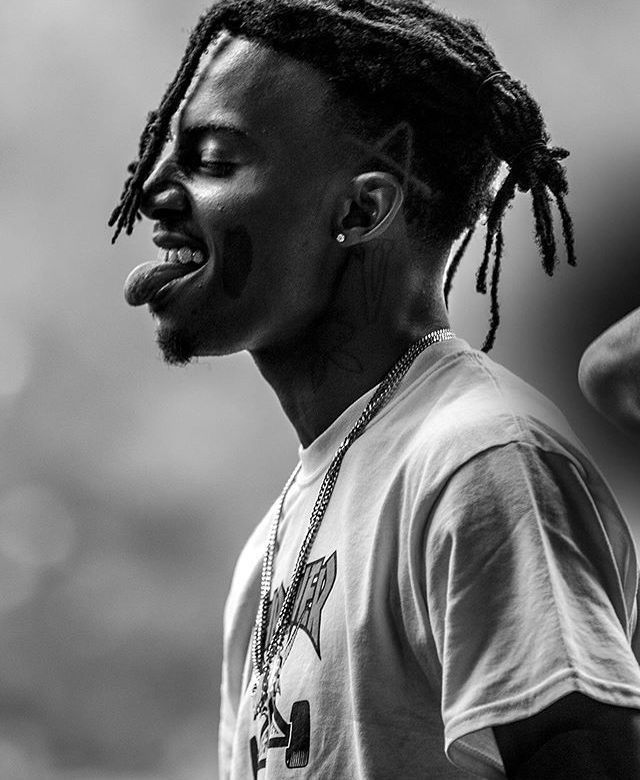 a man with dreadlocks standing in front of a crowd and making a funny face