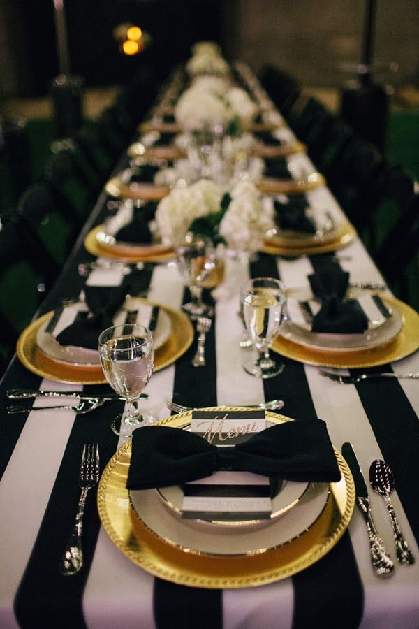 a long table with black and white striped linens, gold plates and silverware