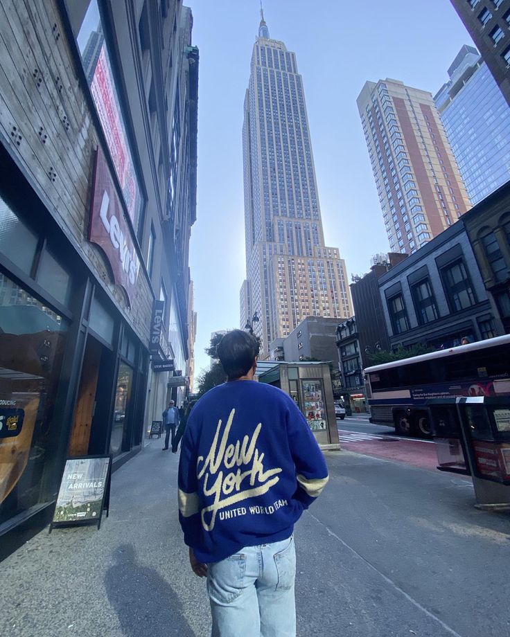 a man is walking down the street in front of tall buildings with skyscrapers behind him