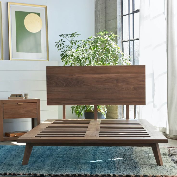 a wooden bed frame sitting on top of a blue rug in front of a window