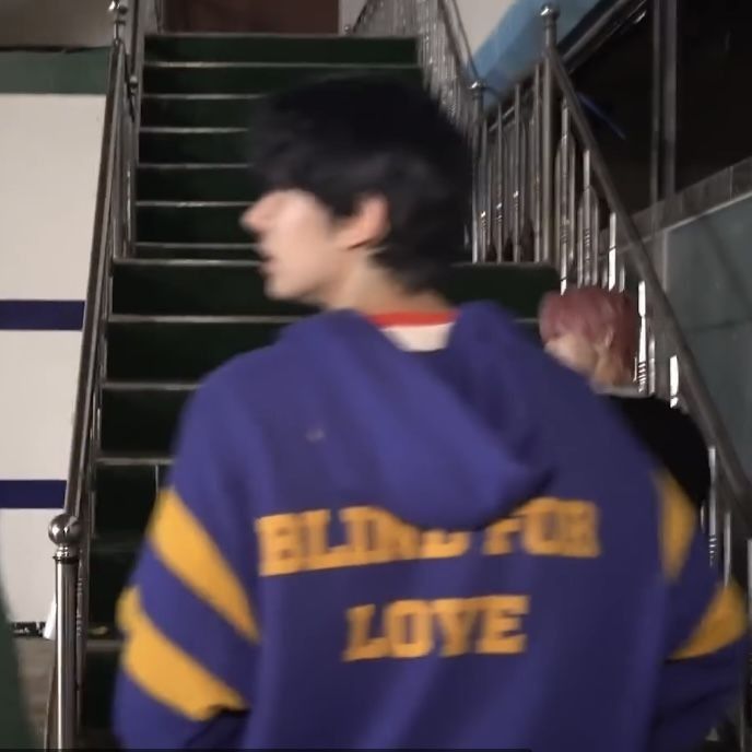 a young man wearing a blue and yellow hoodie walking up stairs with his hand in his pocket