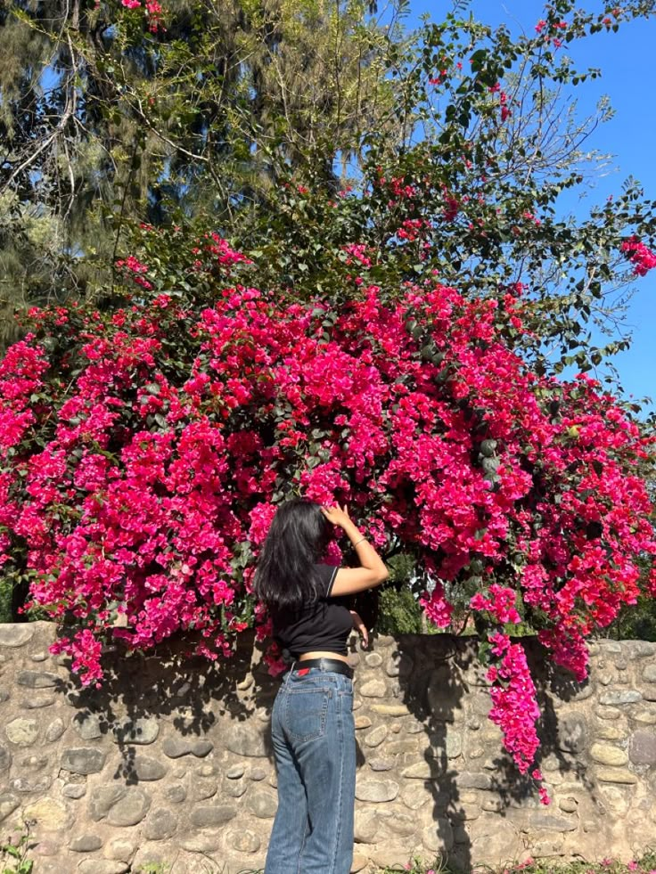 a woman standing in front of a tree with pink flowers