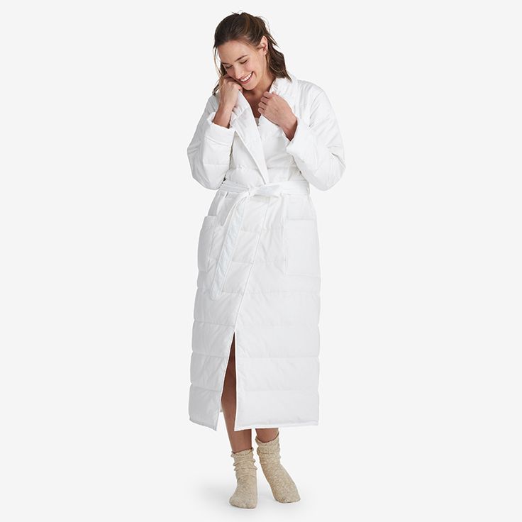 a woman in a white bathrobe is standing with her hand on her face