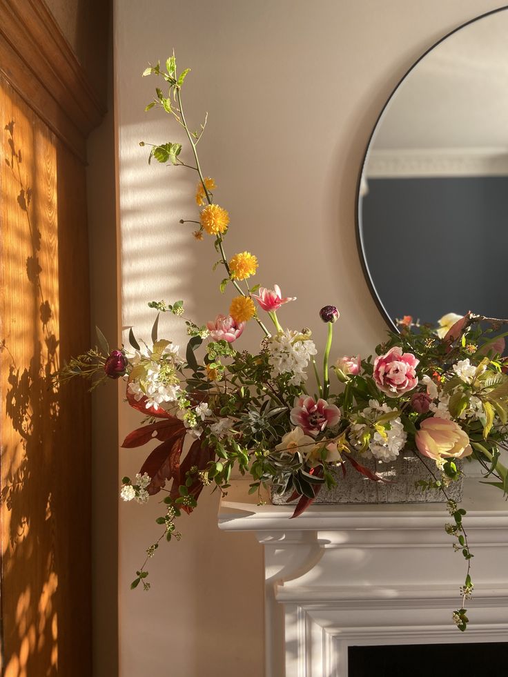 a mirror is above a fireplace with flowers on it