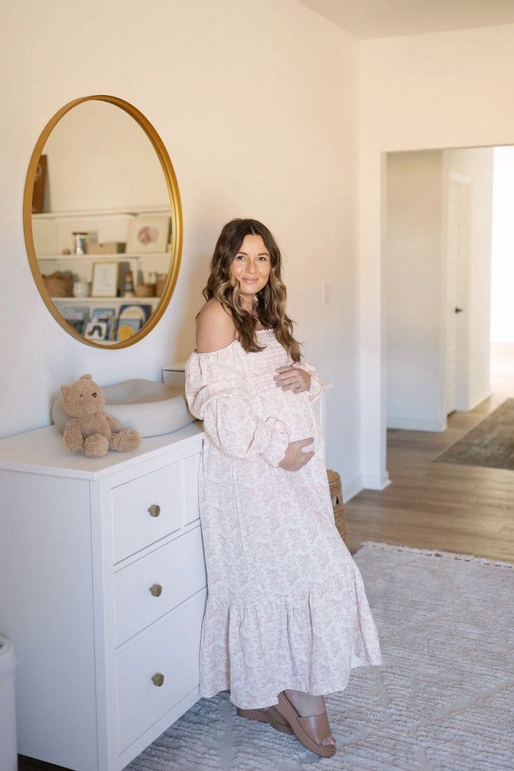 a woman standing next to a dresser with a mirror on the wall and teddy bear