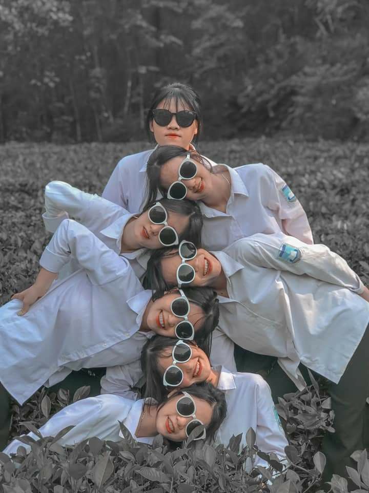 four people are sitting in the grass with sunglasses on their heads and one person is taking a selfie