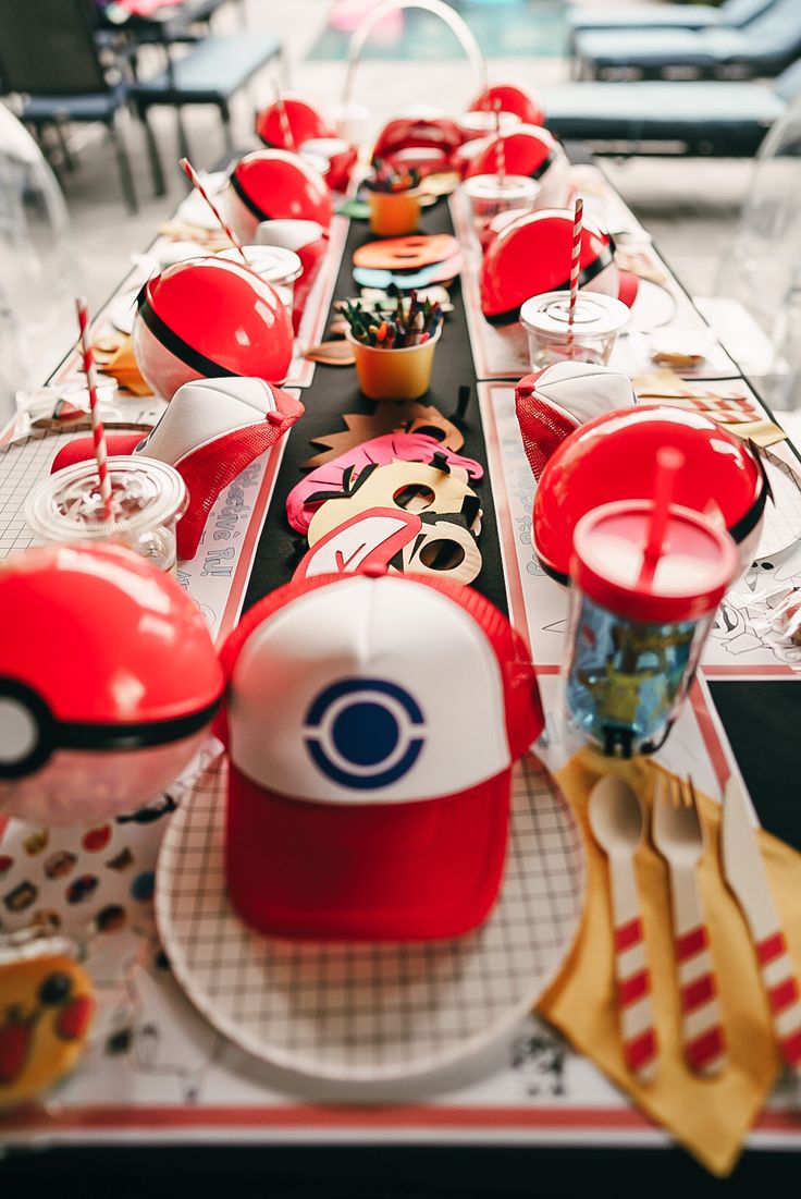 a long table is decorated with red and white plates, cups, and pokemon hats