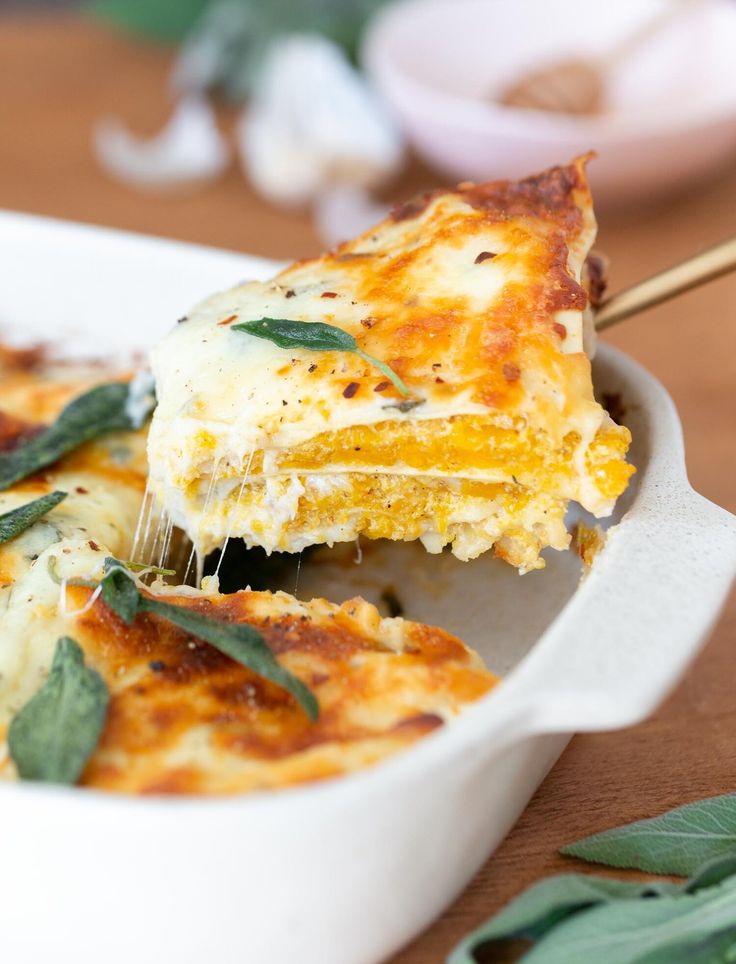 a slice of lasagna being lifted from a white casserole dish on a wooden table