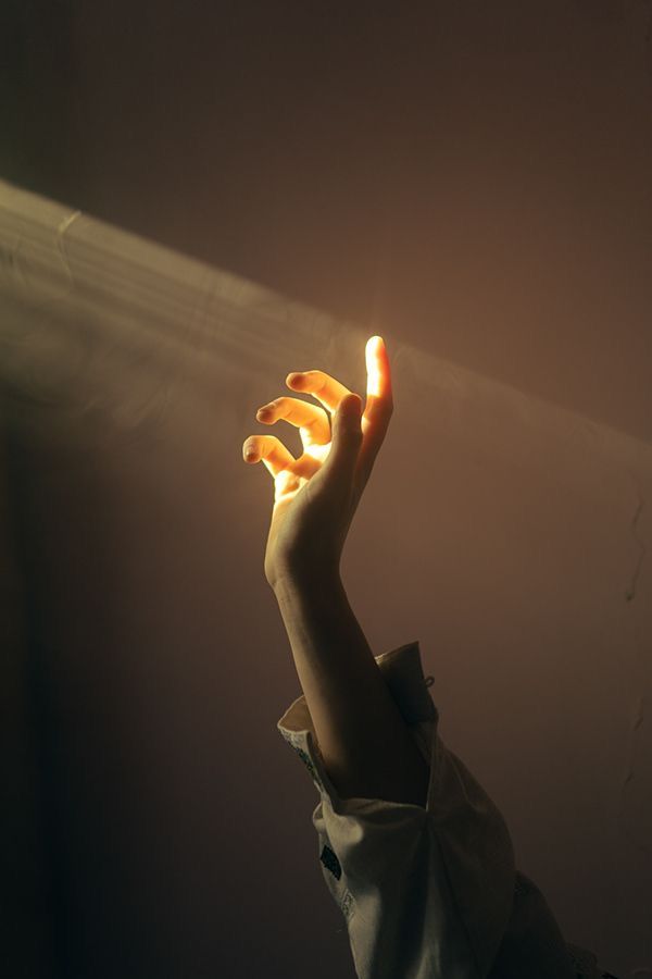 a person holding their hand up in the air with light coming from behind them on a dark background