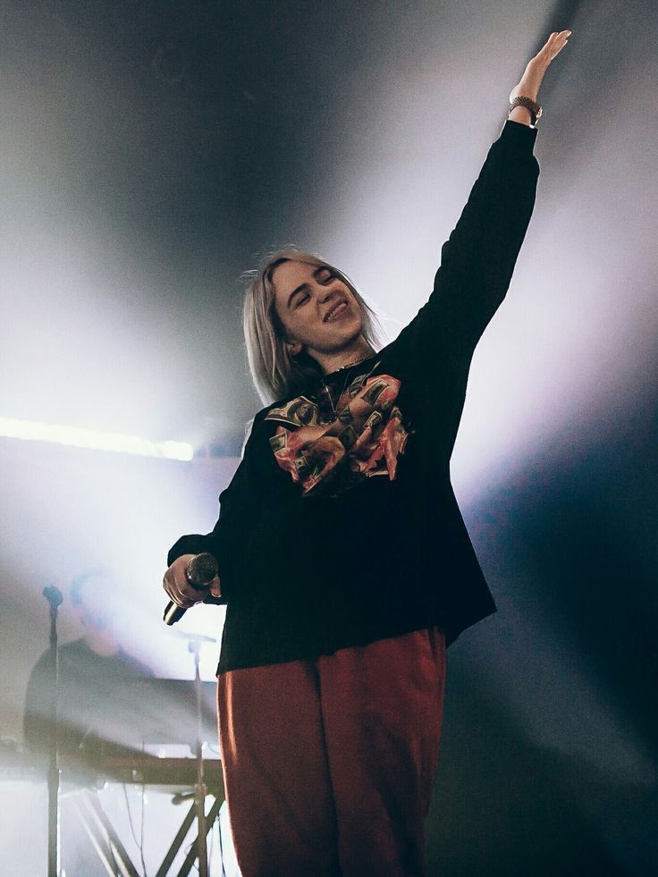 a woman standing on top of a stage with her arms in the air and lights behind her