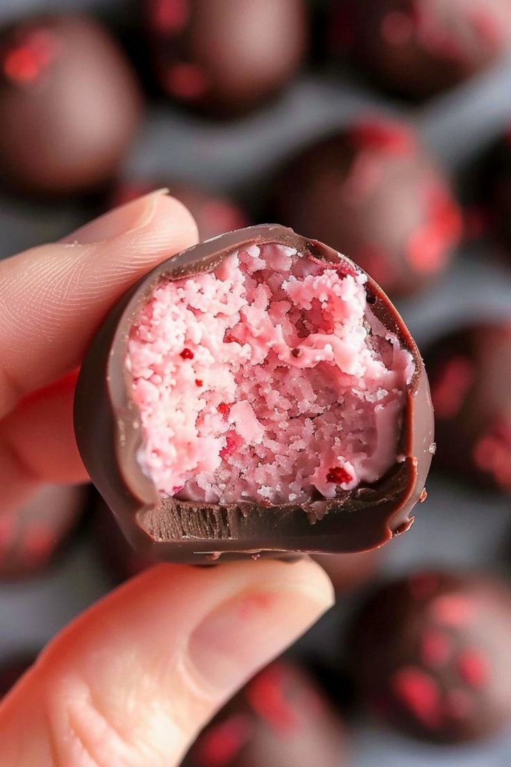 a hand holding a piece of chocolate covered in pink frosting