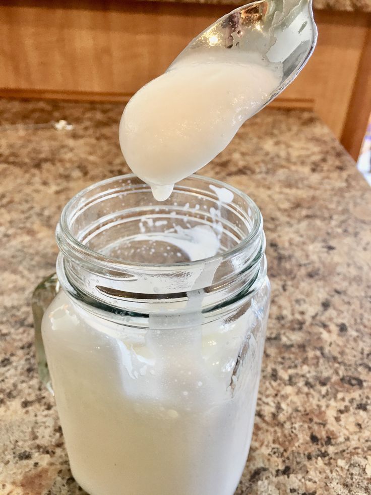 a spoon full of milk being poured into a glass jar on top of a counter