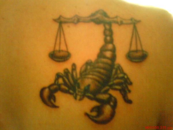 a scorpion tattoo on the back of a woman's shoulder with scales in front of it