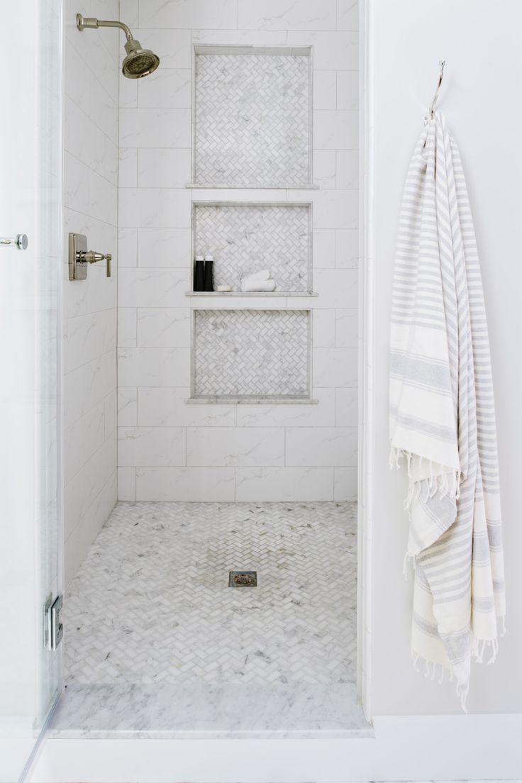 a white bathroom with marble flooring and shelves on the wall, along with a towel rack