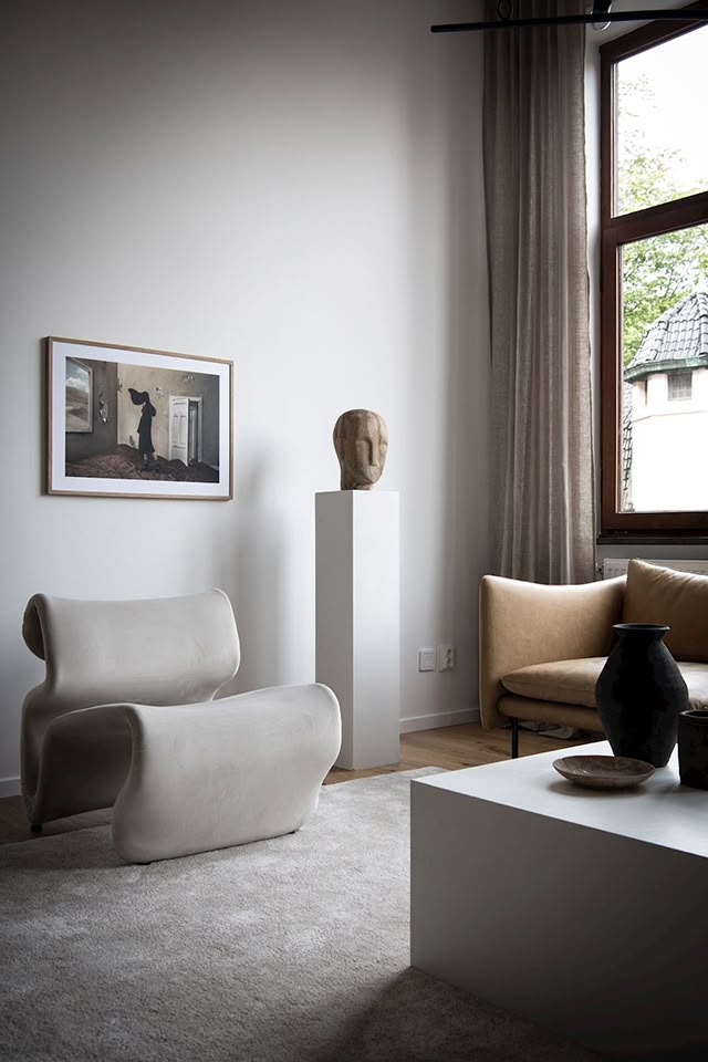 a living room filled with furniture and a large window next to a white table topped with a vase