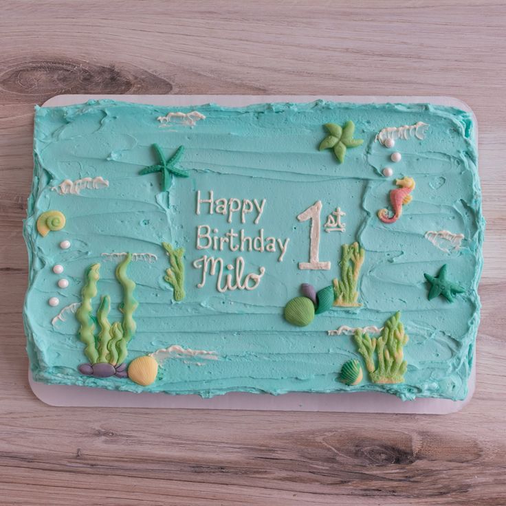 a birthday cake with blue frosting and sea creatures on it, sitting on a wooden table