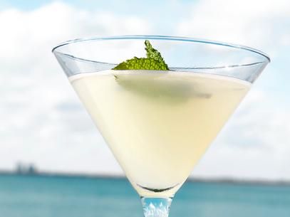 a drink in a martini glass with a mint garnish on the rim and water in the background