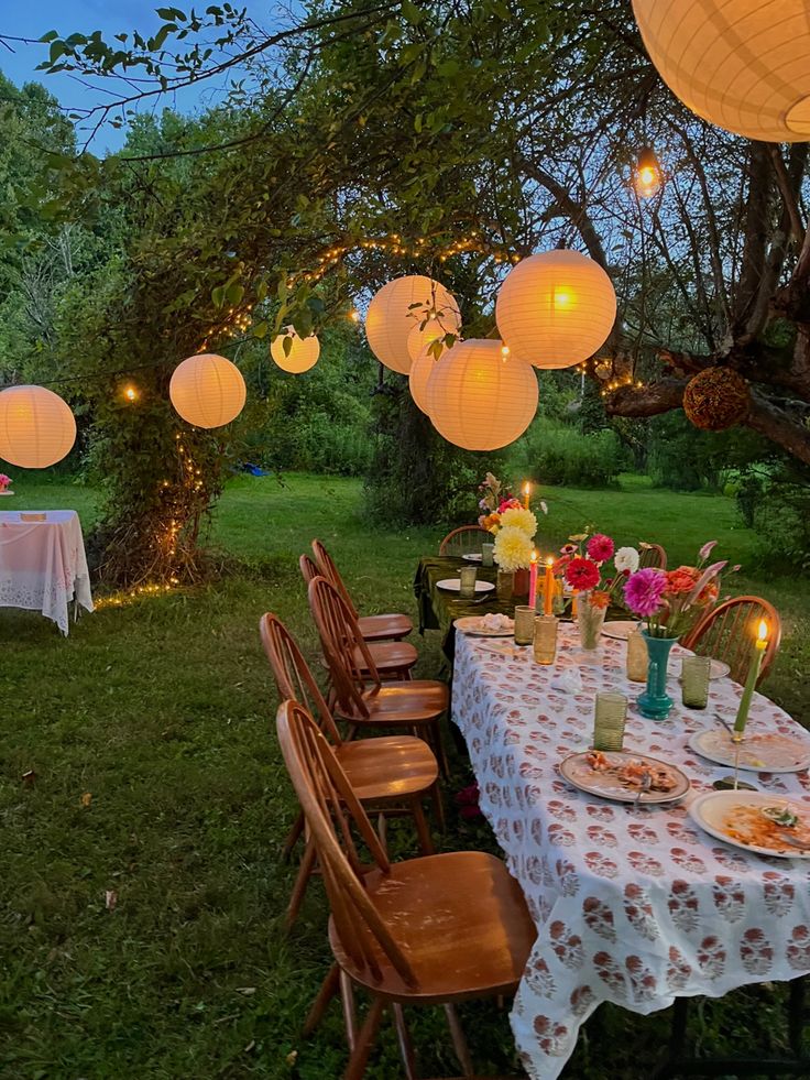 an outdoor dining area with paper lanterns strung from the trees and tables set for dinner