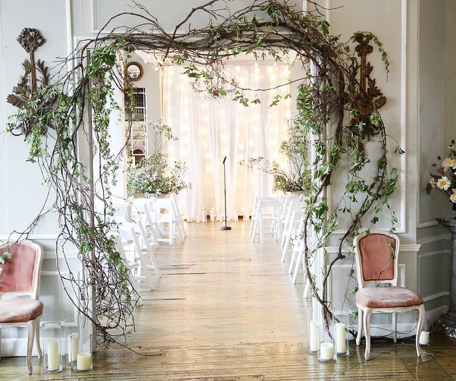 an indoor wedding ceremony with white chairs and greenery on the wall, decorated in pink