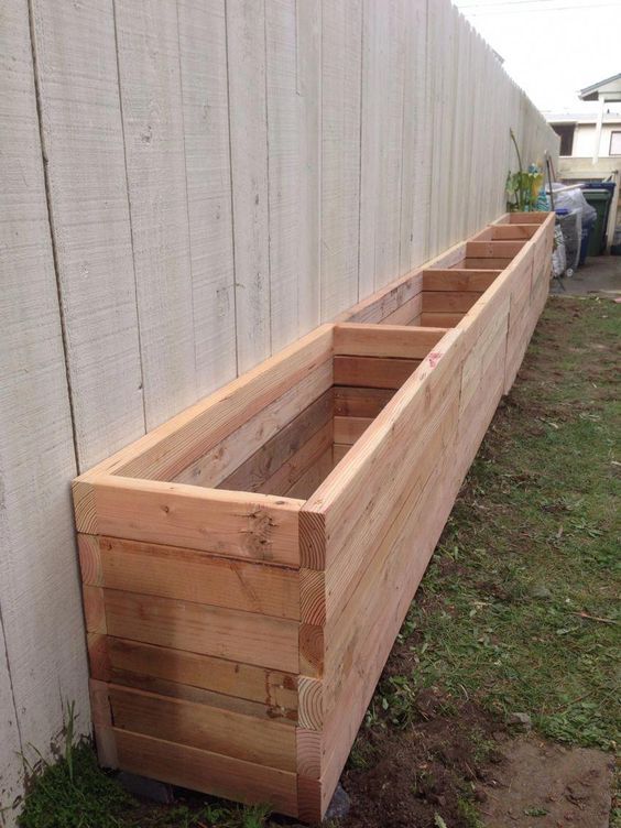 three wooden planters sitting on the side of a white wall next to a grass covered yard