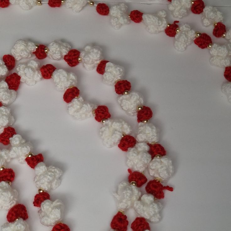 a crocheted necklace with red and white flowers on it is laying on a table