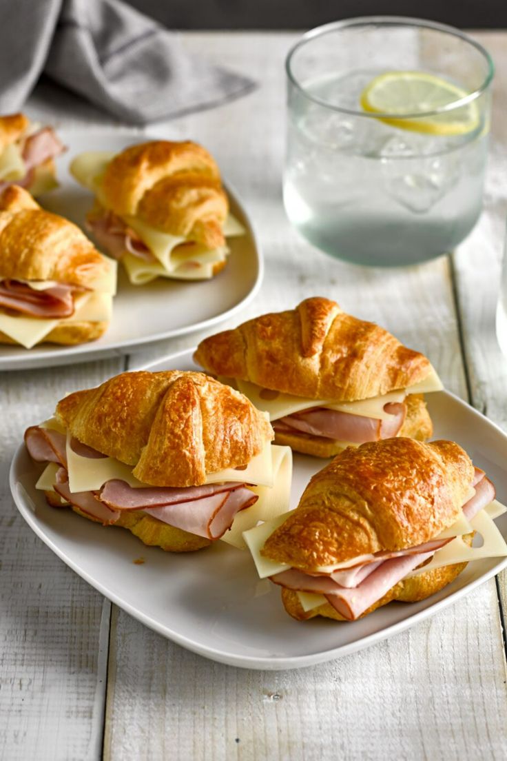 A plate with croissants filled with sliced ham and cheese on a table. Meat And Cheese Croissant, Mini Croissants Sandwiches, Ham And Cheese Mini Croissant, Food With Croissants, Party Croissant Sandwiches, Ham Cheese Croissant Sandwiches, Fillings For Croissants, Brunch Ideas Croissant, Filled Croissants Savory