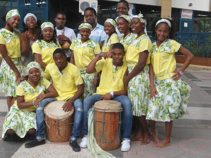 a group of people in yellow dresses posing for a photo with drums and drum sticks