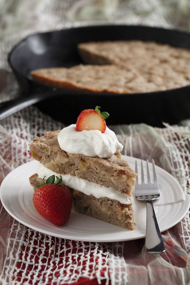 a piece of cake with whipped cream and strawberries on top sits in front of a skillet