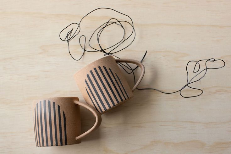 two coffee mugs sitting next to each other on top of a wooden table with wire