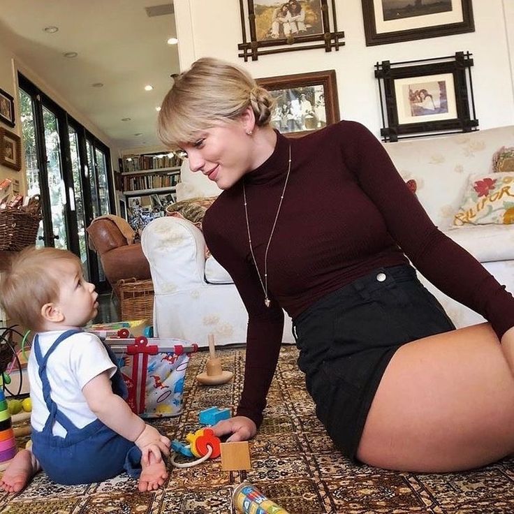 a woman kneeling down next to a baby on top of a rug with toys in front of her