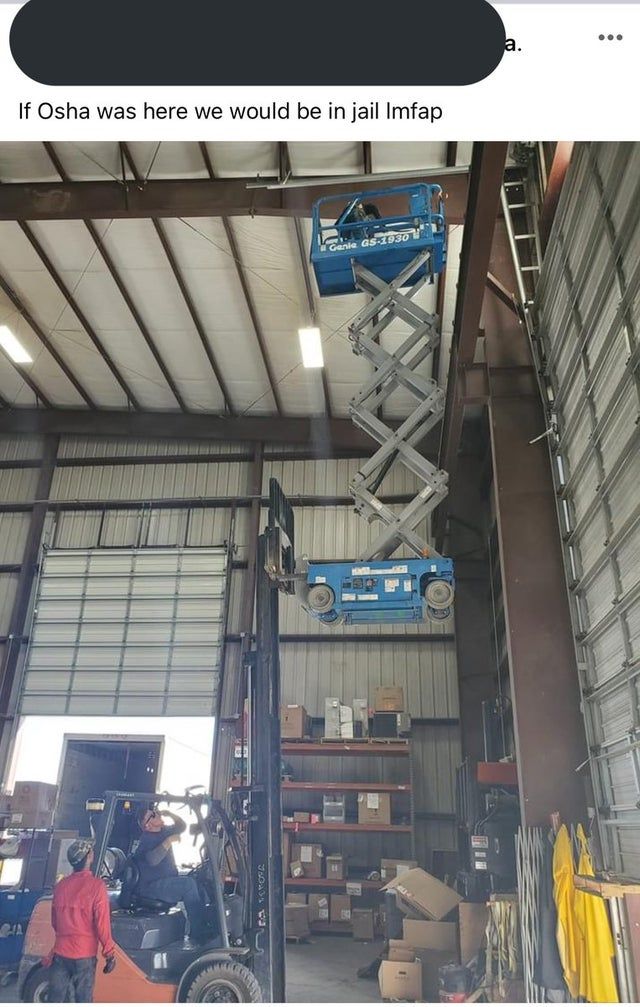 there is a man that is on a lift in the warehouse with other people around him