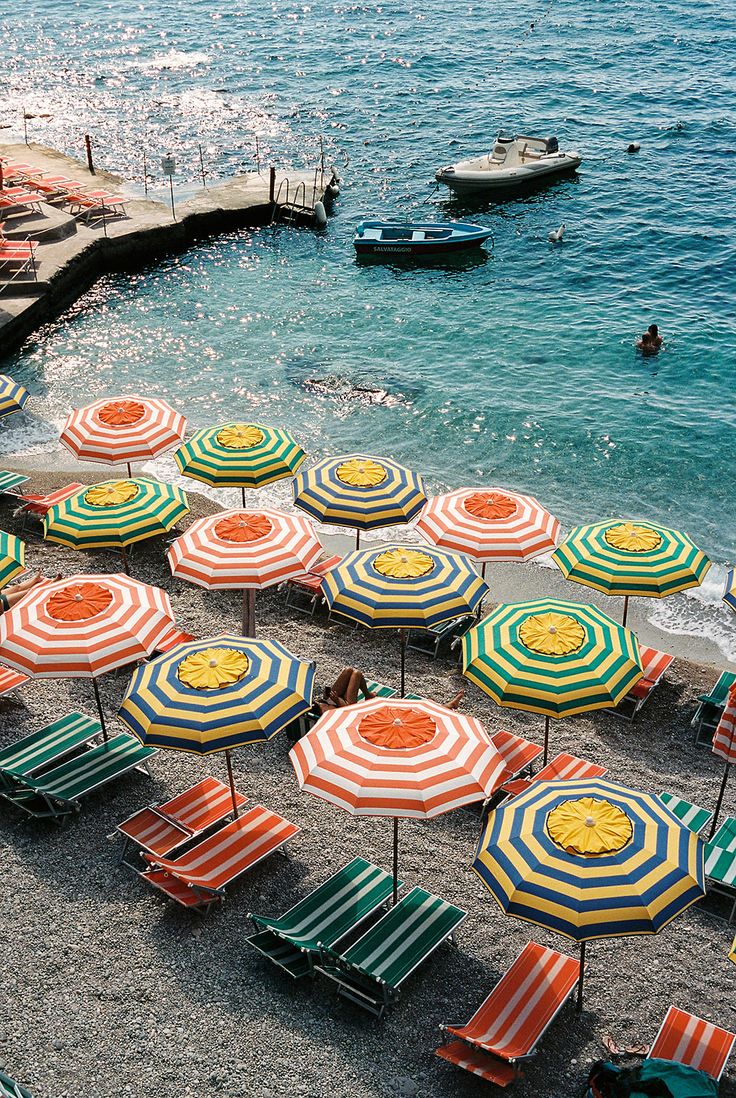 many beach chairs and umbrellas are on the sand near the water's edge