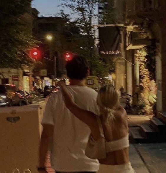 a man and woman walking down the street at night with their arms around each other