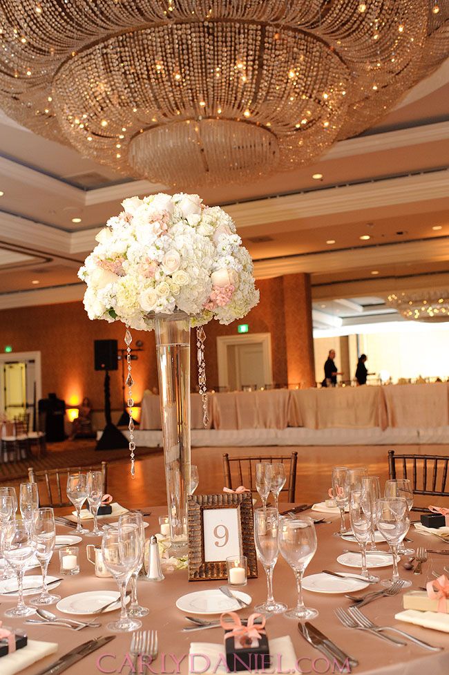 an elegant centerpiece with white flowers in a tall glass vase on top of a table