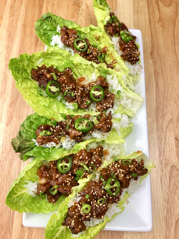 lettuce wraps with meat and rice on a white plate sitting on a wooden table